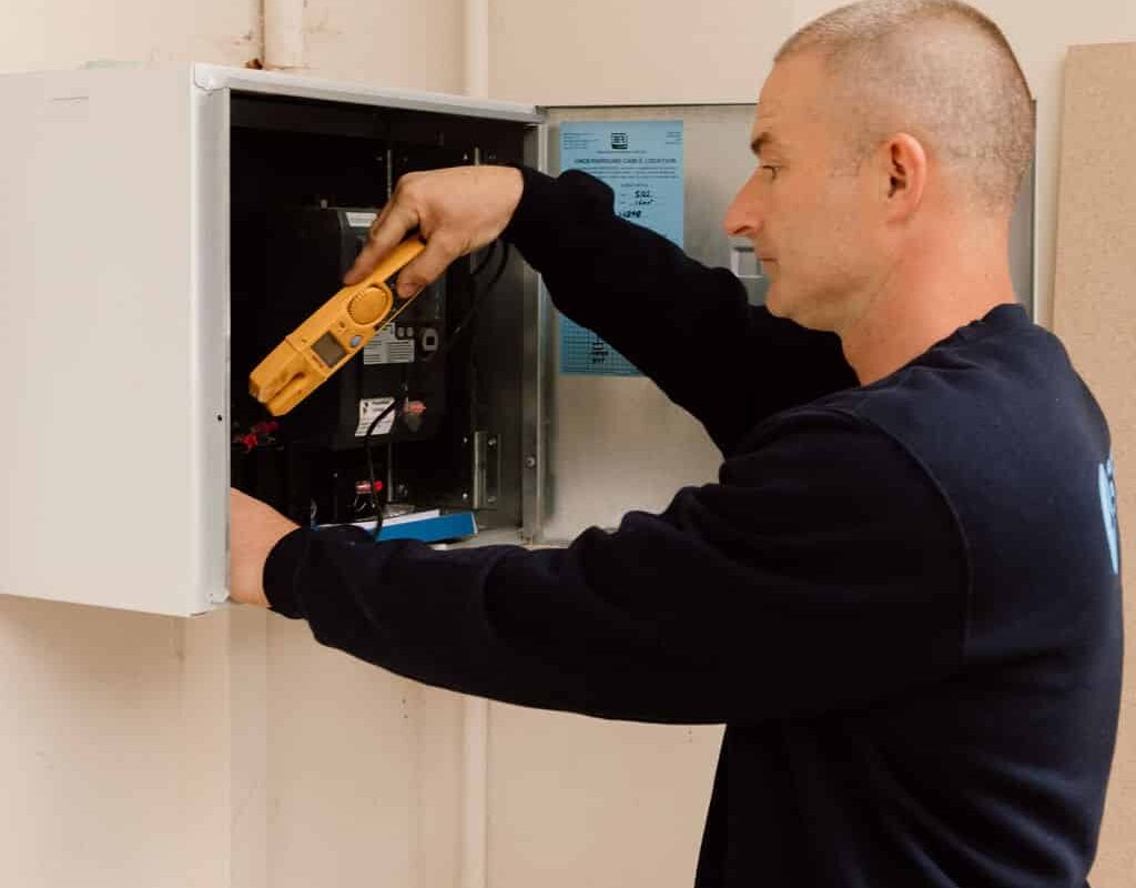 STL Electrical electrician testing the load at a wall mounted switchboard